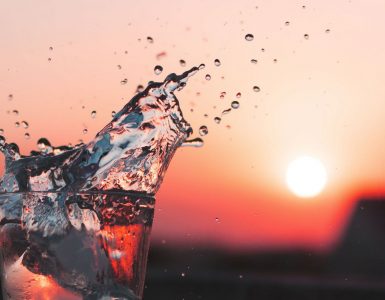 glass of water with ice exploding in front of a sunset